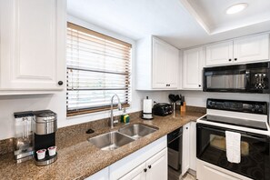 Uma cozinha moderna com armários brancos, bancada de granito, cafeteira, torradeira, micro-ondas e forno.