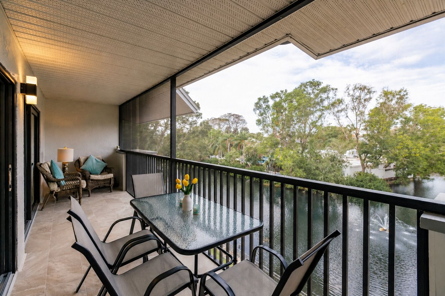 A balcony with a glass table, chairs, and a vase with flowers.