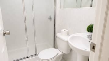 Un baño con inodoro, lavamanos y ducha con mampara de vidrio.