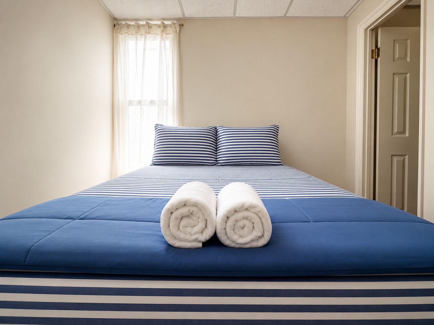 Een hotelkamer met een bed, twee kussens, een raam met gordijnen en een deur.