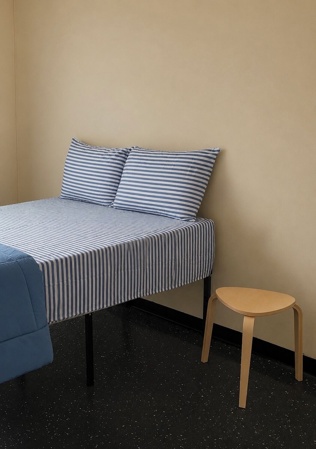 A bed with striped bedding, a small stool, and a plain wall.