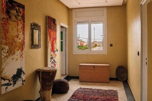 A hallway with a large window, a wooden bench, a drum, and abstract art on the walls. - Seaview Apartment, Balcony, Great Location (Mirleft)