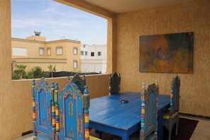 A room with a blue table and chairs, a painting on the wall, and a view of buildings outside. - Seaview Apartment, Balcony, Great Location (Mirleft)