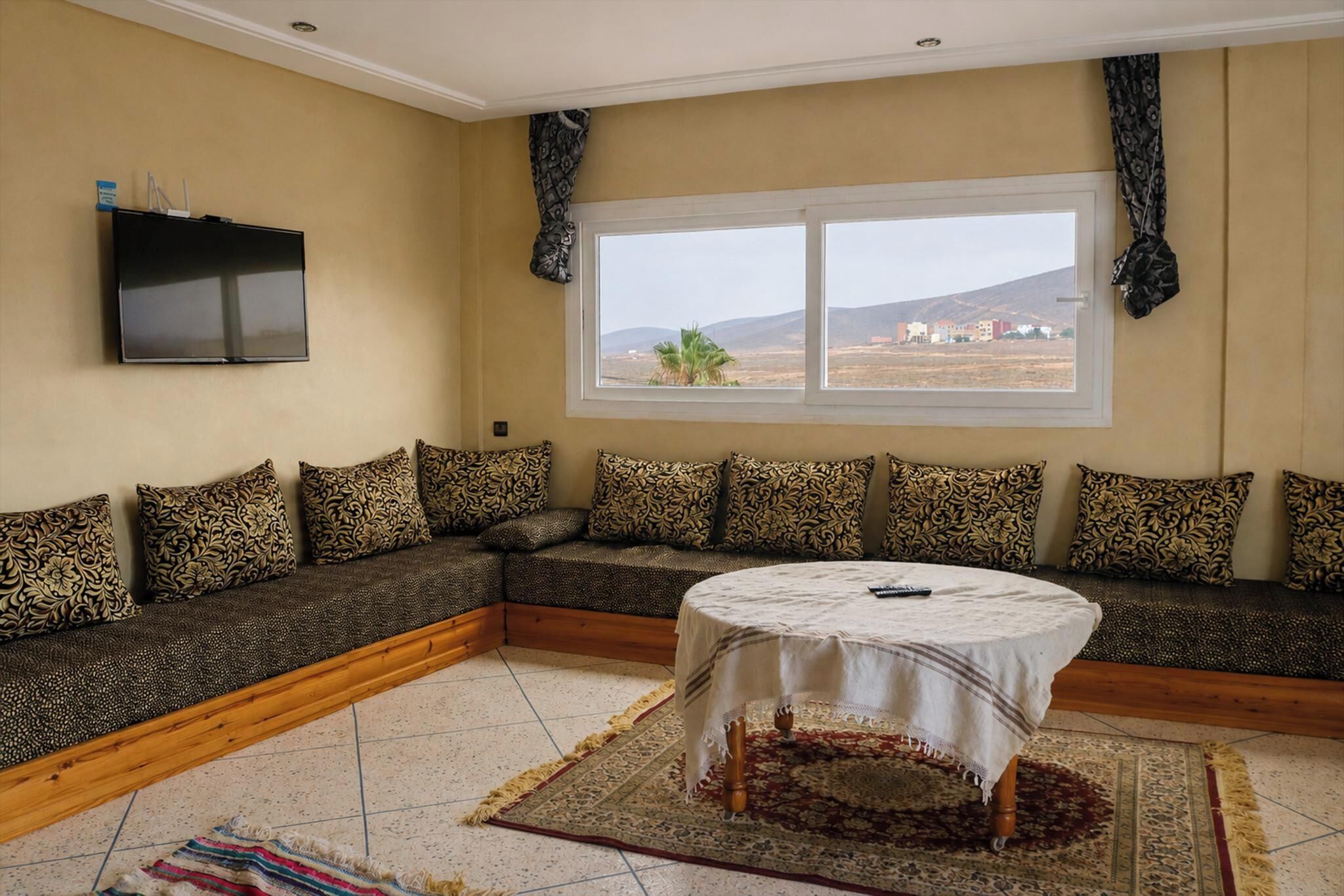 A living room with a sofa, a TV, a window, and a round table.