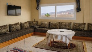 A living room with a sofa, a TV, a window, and a round table. - Seaview Apartment, Balcony, Great Location (Mirleft)