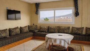 A living room with a sofa, a TV, a window, and a round table.
