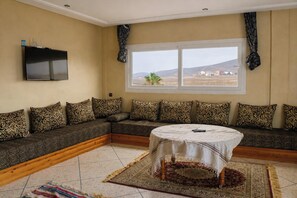 A living room with a sofa, a TV, a window, and a round table. - Seaview Apartment, Balcony, Great Location (Mirleft)