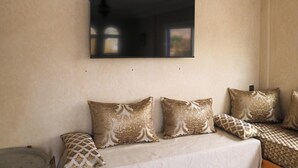 A room with a large flat-screen TV mounted on the wall, a sofa with patterned cushions, and a bed with a patterned bedspread.