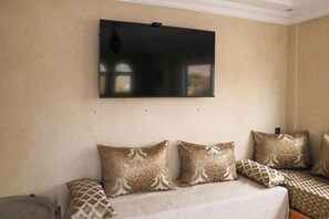 Une pièce dotée d’un grand téléviseur à écran plat fixé au mur, d’un canapé agrémenté de coussins à motifs et d’un lit recouvert d’une couvre-lit à motifs.