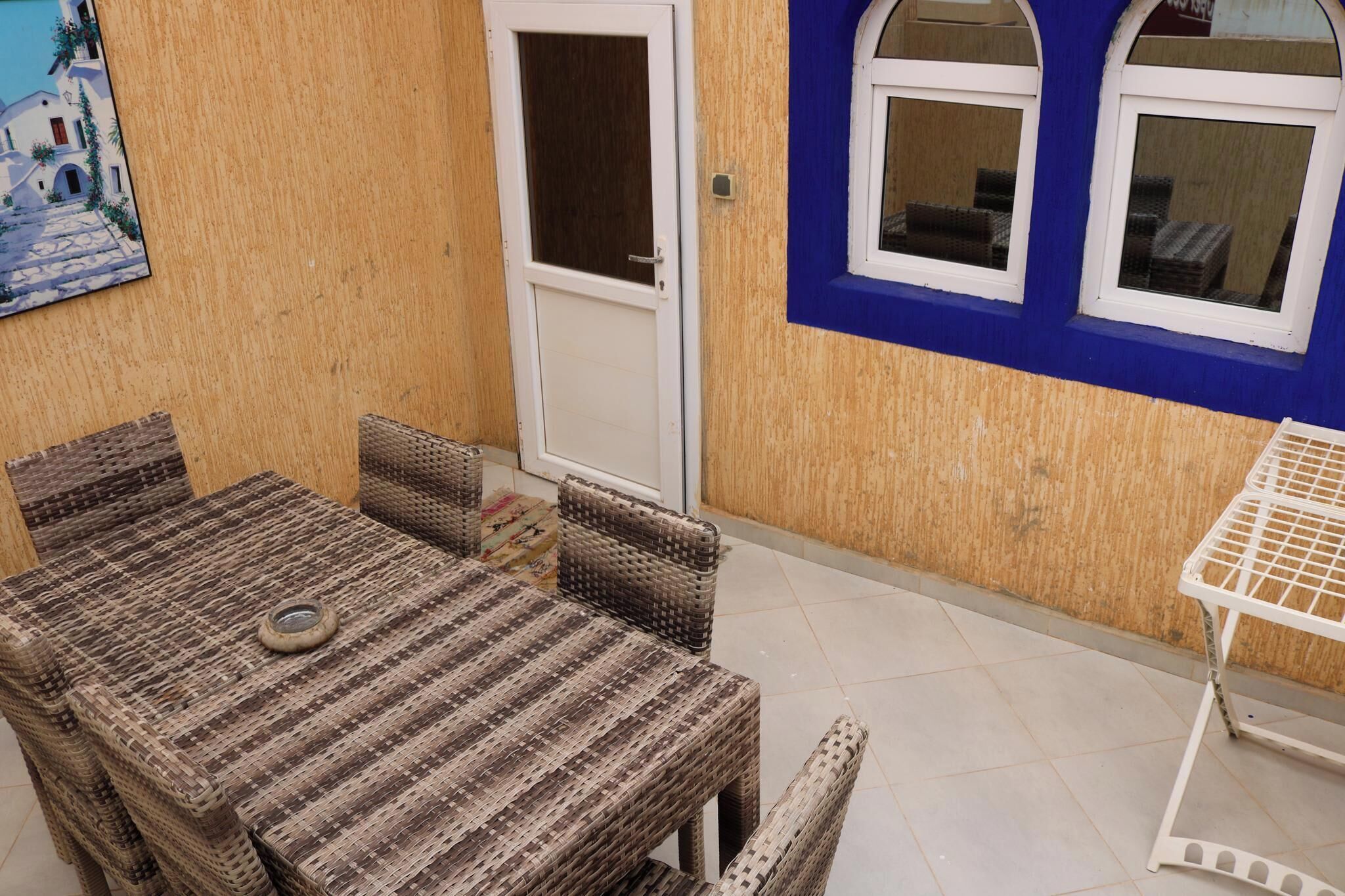A room with a wicker table and chairs, a white door, and a blue wall with windows.