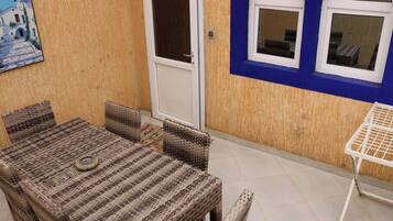 A room with a wicker table and chairs, a white door, and a blue wall with windows.