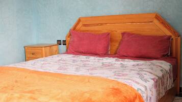 A bedroom with a wooden headboard, two pillows, a nightstand, and a floral bedspread.