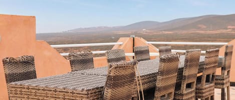 A rooftop terrace with wicker furniture and a view of distant hills.