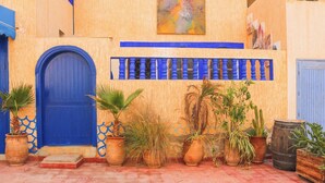 A building with a blue door, potted plants, and a wooden barrel.