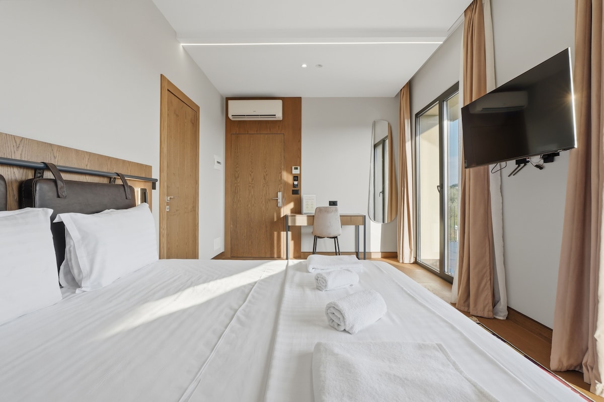 Habitación de hotel con cama, escritorio, silla, televisor y ventana con cortinas.