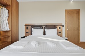 A hotel room with a wooden headboard, a bedside table with a phone, and a wardrobe with hanging robes. - Prelude Boutique Country Hotel (Manez)