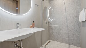 Ett modernt badrum med en vit tvättställ, en duschkabin i glas och en spegel med en rund lampa.
