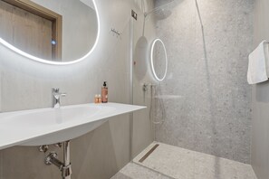 Un baño moderno con un lavamanos blanco, una cabina de ducha de vidrio y un espejo con luz circular.