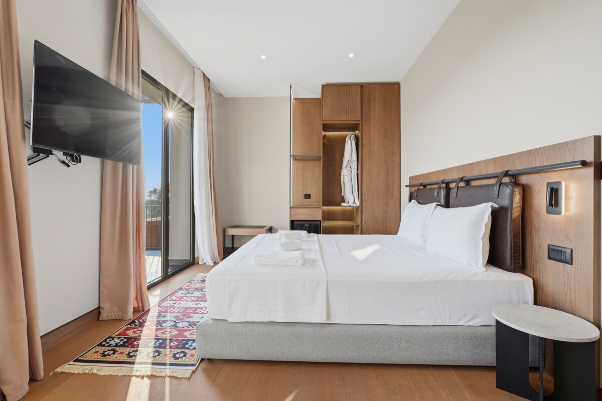 Una habitación de hotel con una cama grande, un televisor de pantalla plana montado en la pared, un armario de madera y una mesita pequeña.