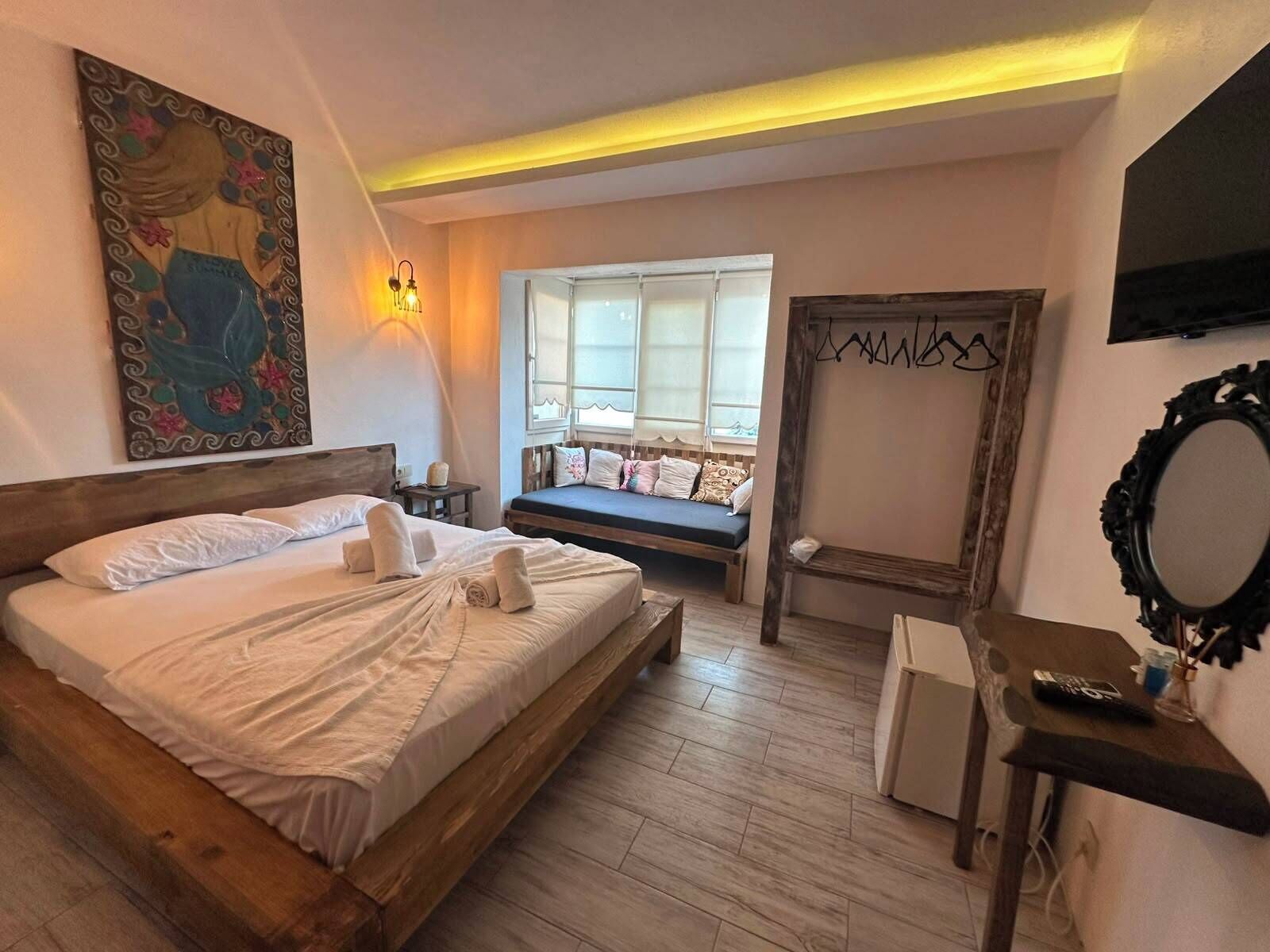Una camera da letto con un letto grande, un comodino, una panca, uno specchio e una televisione.