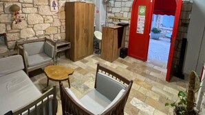 Um quarto com paredes de pedra, uma mesa de madeira com cadeiras, uma porta vermelha e um candeeiro pendurado.