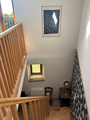 Eine Holztreppe mit einem kleinen Fenster, einem gerahmten abstrakten Kunstwerk und einer Wand mit Muster.