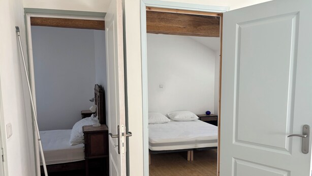 Ein Zimmer mit einem Bett, einem Schreibtisch und einem Stuhl. Eine Tür führt in einen weiteren Raum.