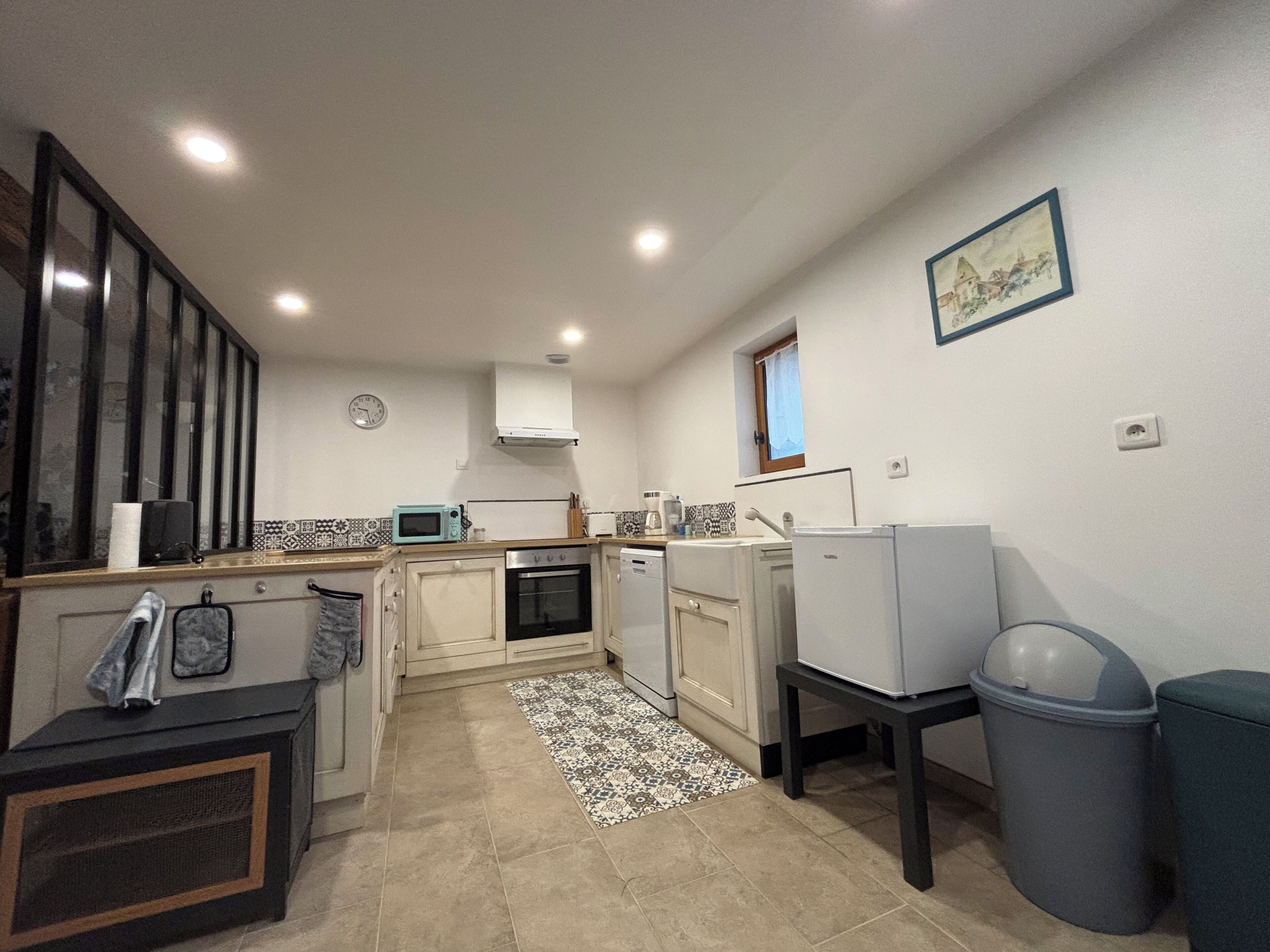 A compact kitchen with a microwave, oven, and sink. There is a small window and a clock on the wall.