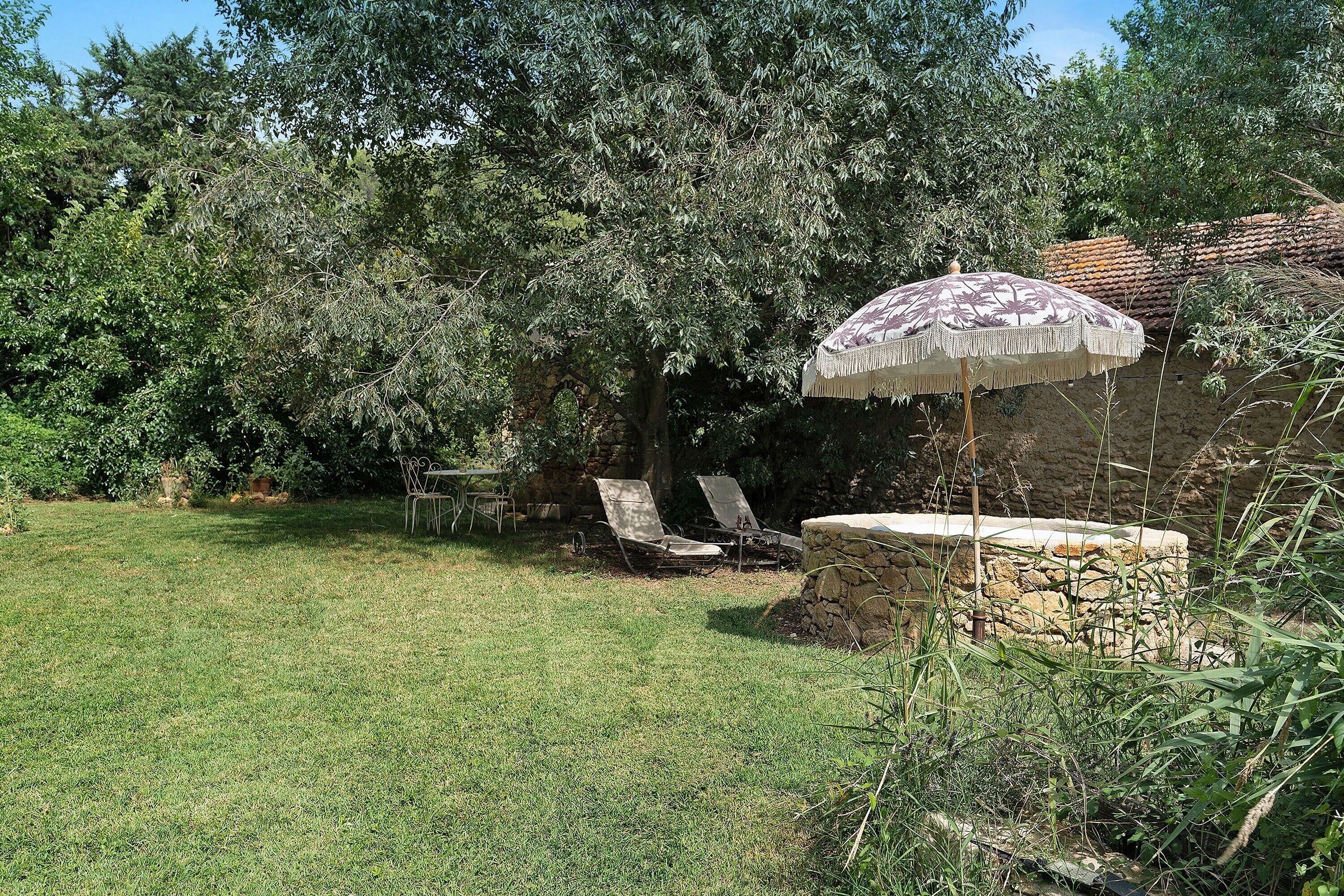 Un jardin avec un banc en pierre, une table et une chaise sous un arbre.