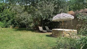 Un jardin avec un banc en pierre, une table et une chaise sous un arbre.