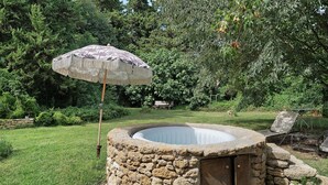 A stone hot tub with a wooden door, surrounded by a stone wall, in a lush garden with dense foliage. - Holiday Home 'Maison En Pierre Chevaux' with Wi-Fi (Puyvert)