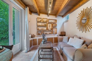 Un salon chaleureux avec un plafond en bois, un canapé, une table basse et un grand miroir rond accroché au mur.