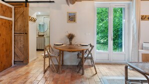 A rustic dining area with a wooden table, chairs, and a view through a glass door. - Holiday Home 'Maison En Pierre Chevaux' with Wi-Fi (Puyvert)