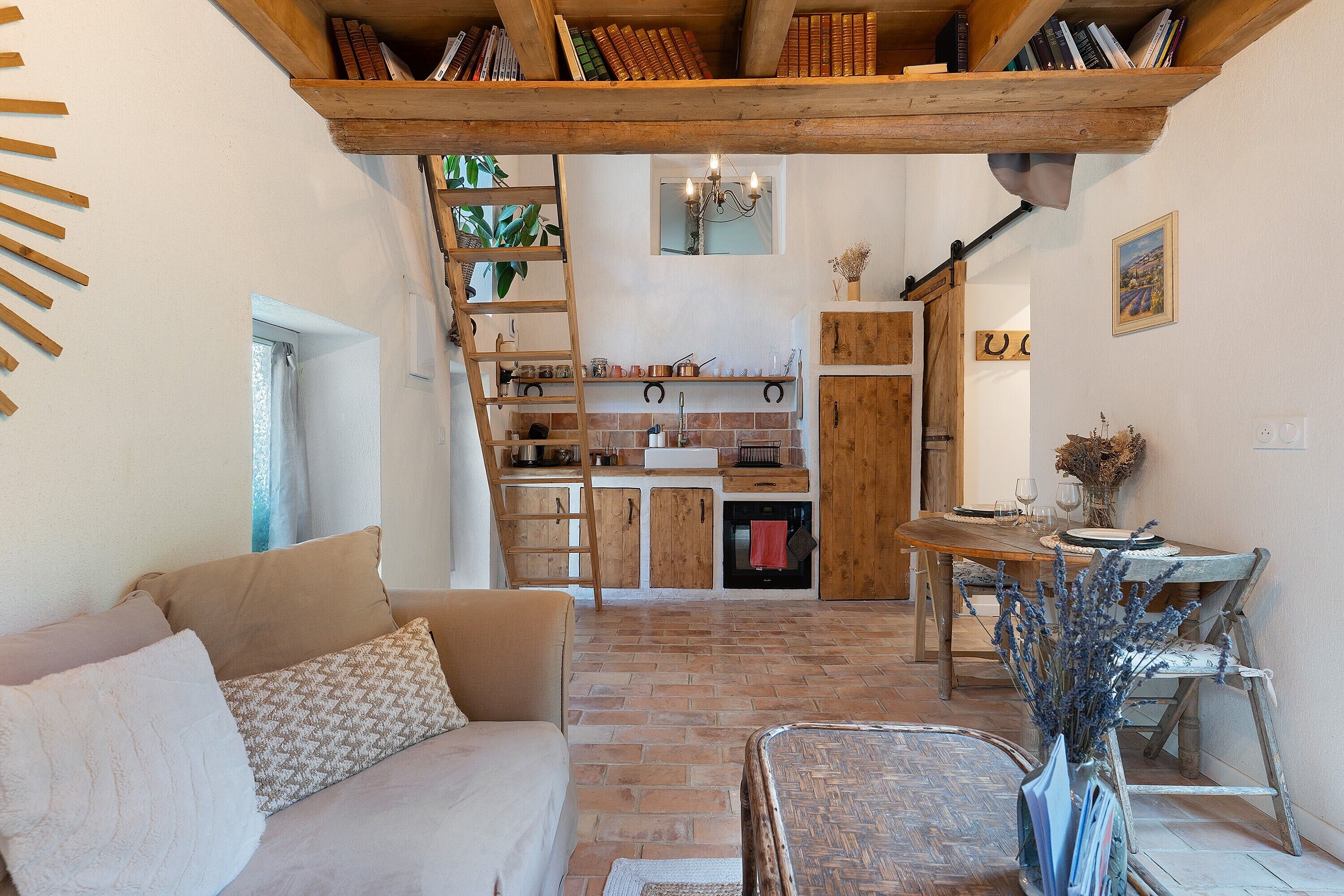 Un salon chaleureux avec un escalier en bois, une cuisine avec un mur de crédence en briques et une table à manger dressée pour deux personnes.