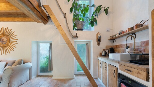 A kitchen with a brick floor, wooden cabinets, a hanging plant, and a sunburst mirror. - Holiday Home 'Maison En Pierre Chevaux' with Wi-Fi (Puyvert)