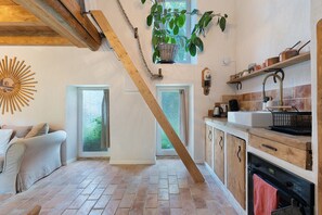 A kitchen with a brick floor, wooden cabinets, a hanging plant, and a sunburst mirror.