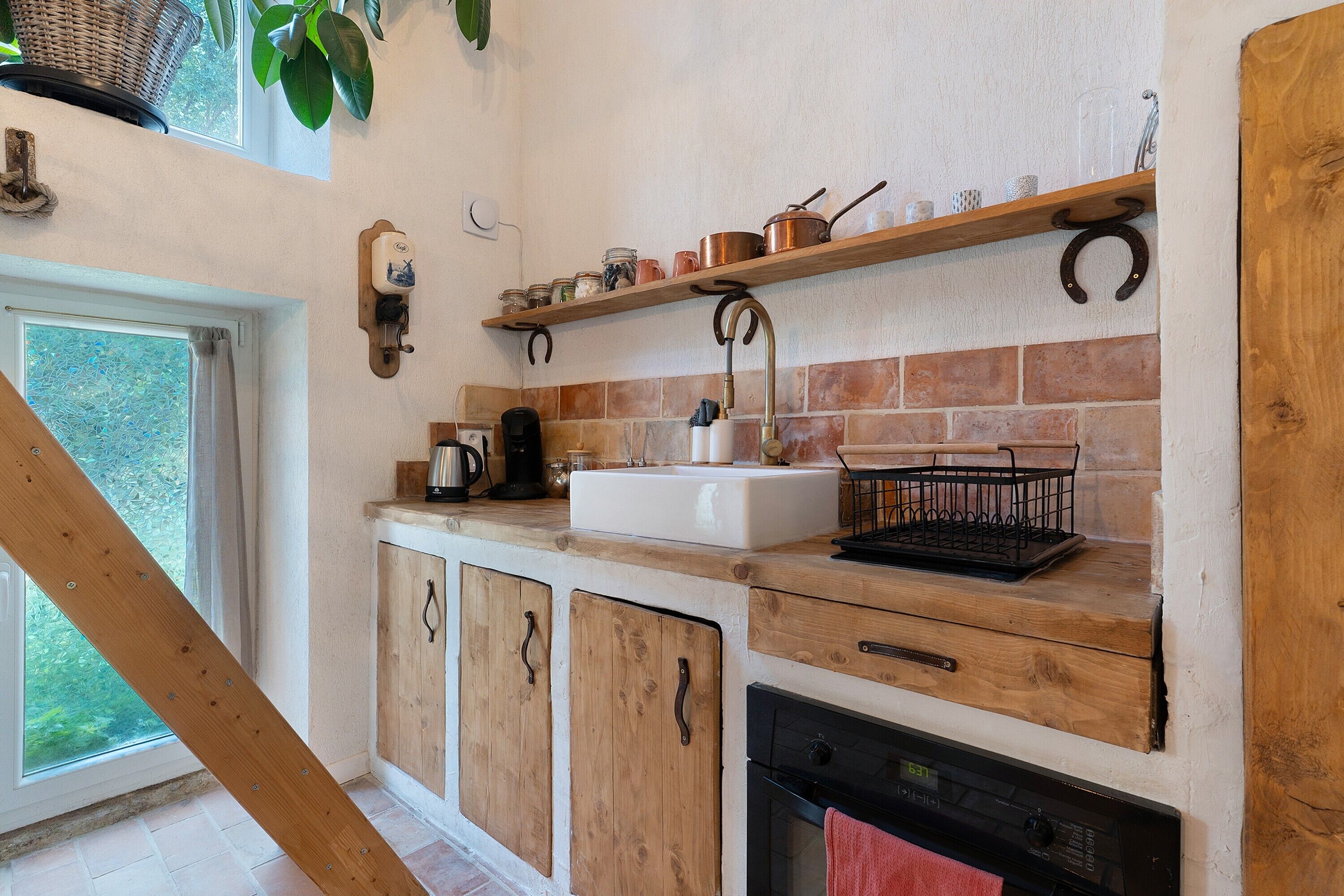 Une cuisine avec un mur de fond en briques, des armoires en bois, un évier et une machine à café.