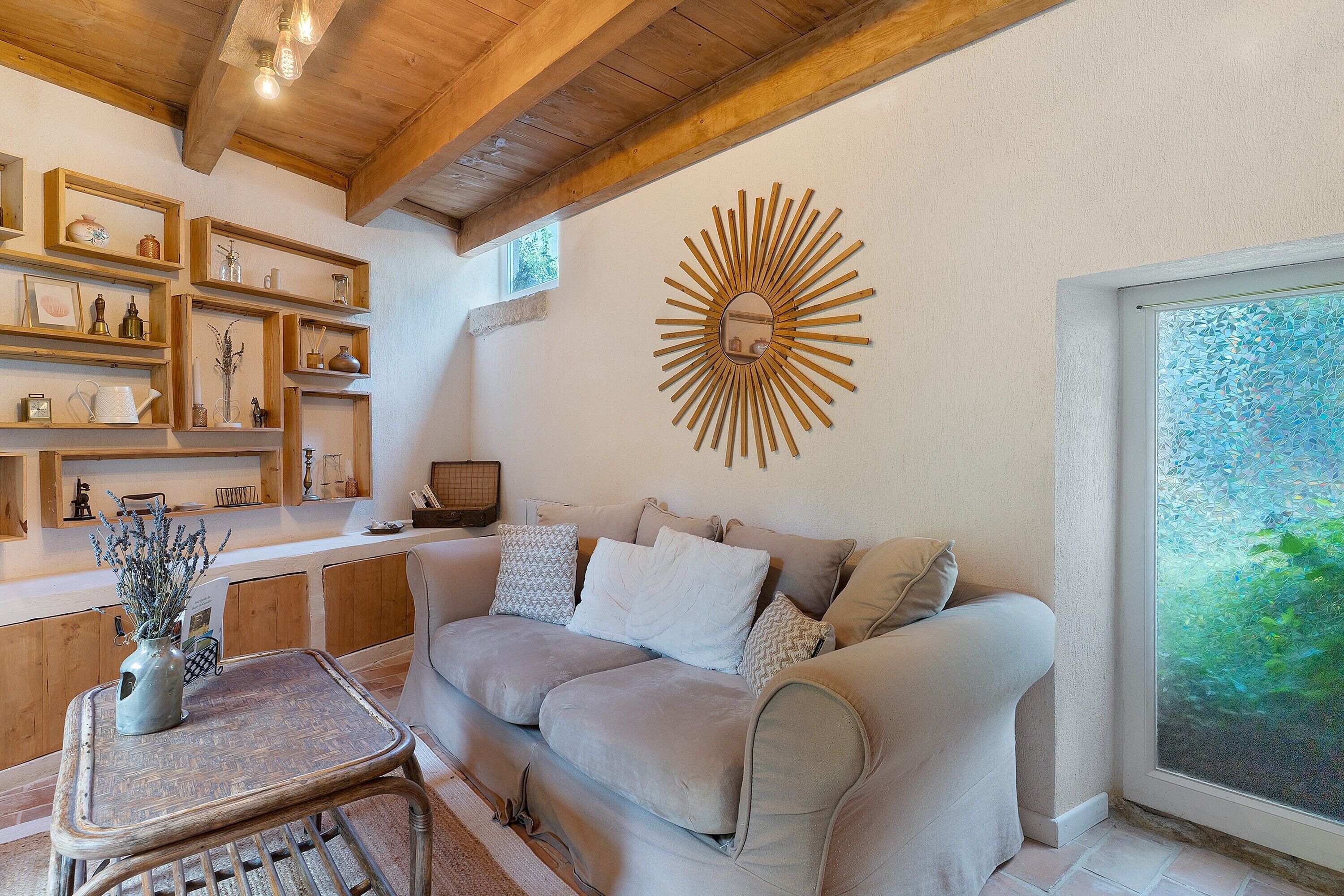 Un salon chaleureux avec un plafond en bois, une décoration murale en forme de soleil, un canapé agrémenté de coussins et une table d’appoint sur laquelle est posé un vase.