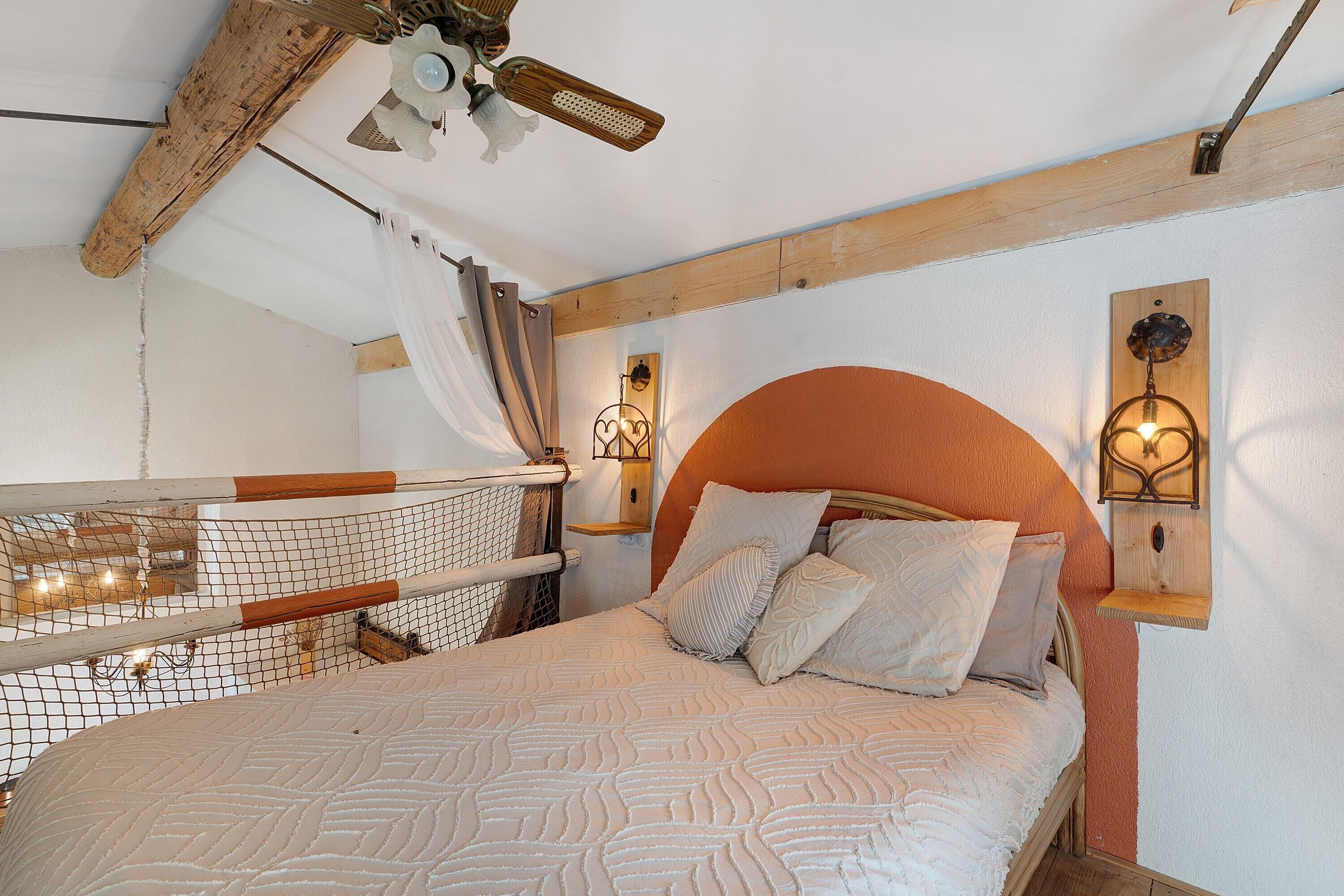 Ein Schlafzimmer mit einem hölzernen Kopfende, einer gemusterten Bettdecke und einem Deckenventilator.