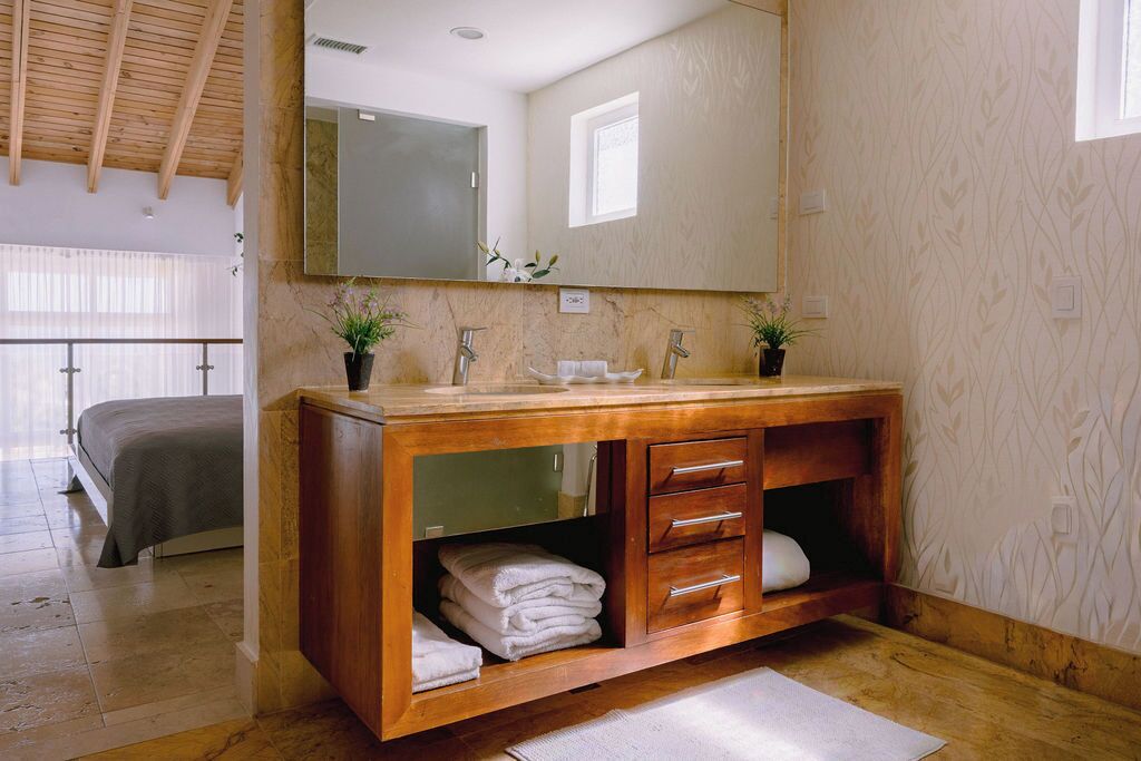 A bathroom with a wooden vanity, a large mirror, and a bed in the adjacent room.