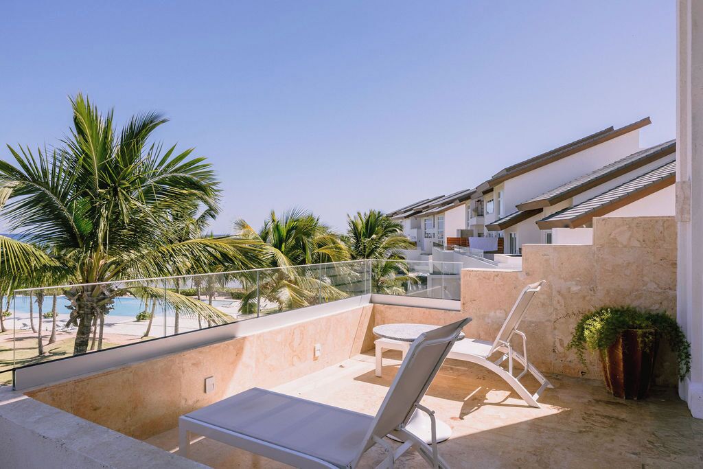 Ein Balkon mit Blick auf einen Pool, eine Liege und eine Treppe, die zu einer erhöhten Ebene führt.