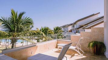 Ein Balkon mit Blick auf einen Pool, eine Liege und eine Treppe, die zu einer erhöhten Ebene führt.