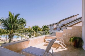 Un balcon avec vue sur la piscine, une chaise longue et un escalier menant à un niveau supérieur.