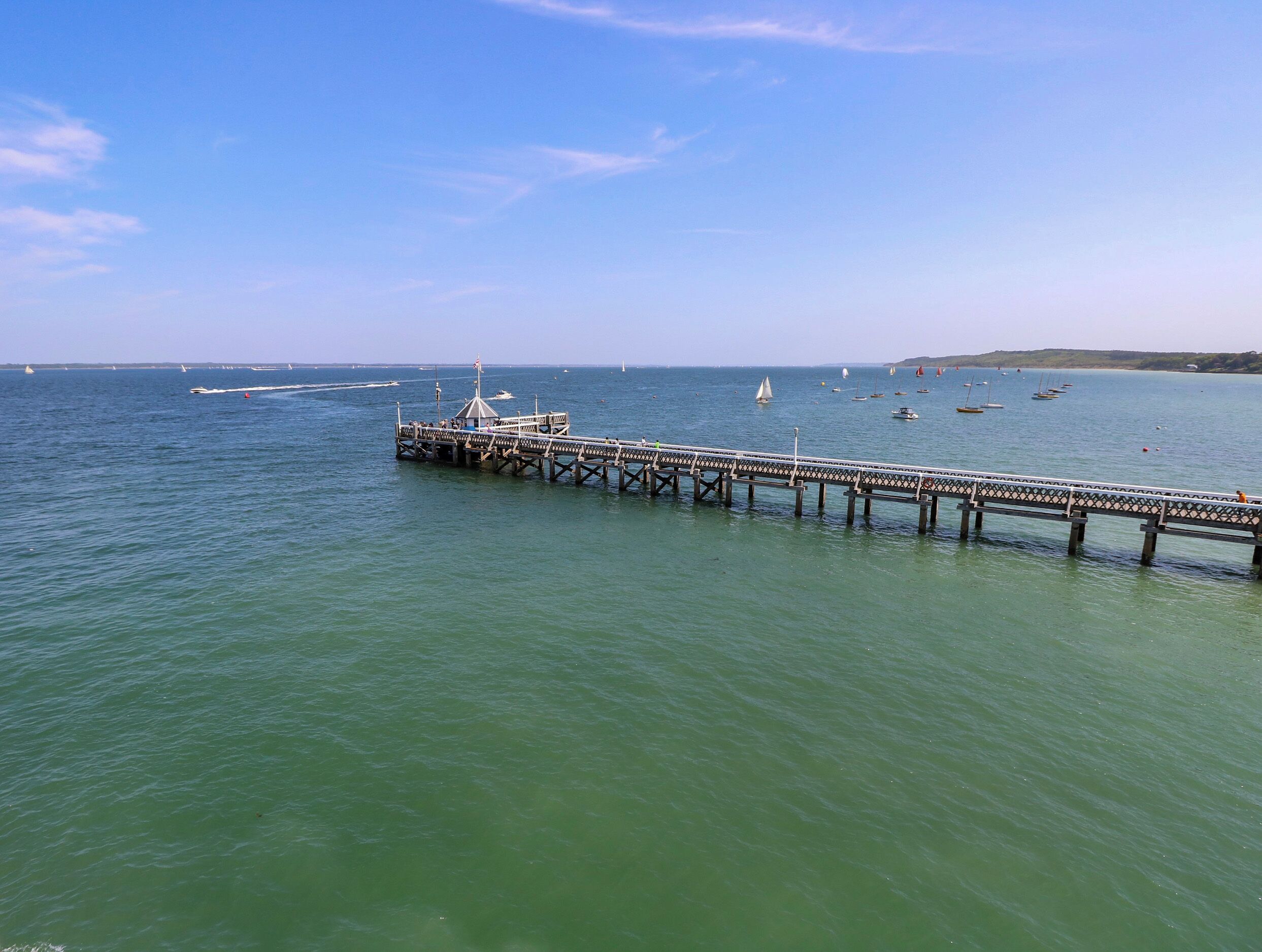 A pier extending into calm waters with boats and a clear sky.