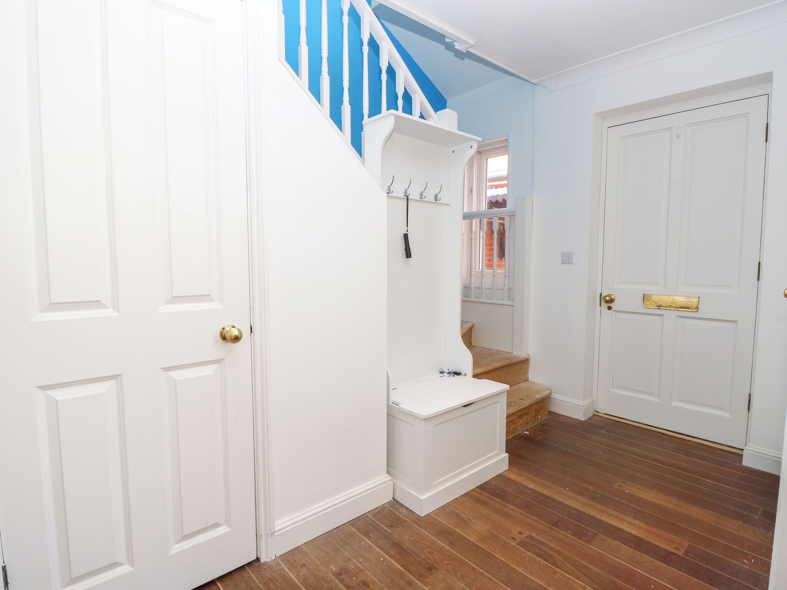 A hallway with white doors, a blue staircase, and a wooden floor.
