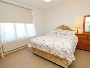 A bedroom with a bed, a dresser, a mirror, and a window with sheer curtains. - Merrilees (Yarmouth)