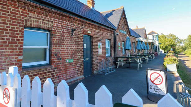 A brick building with a green door, outdoor seating, and a no cycling sign. - Merrilees (Yarmouth)