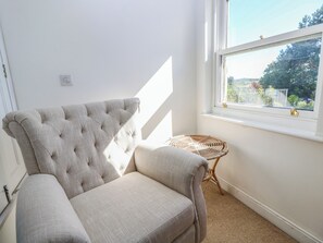 A room with a tufted armchair, a small wicker chair, and a window with a view of greenery. - Merrilees (Yarmouth)