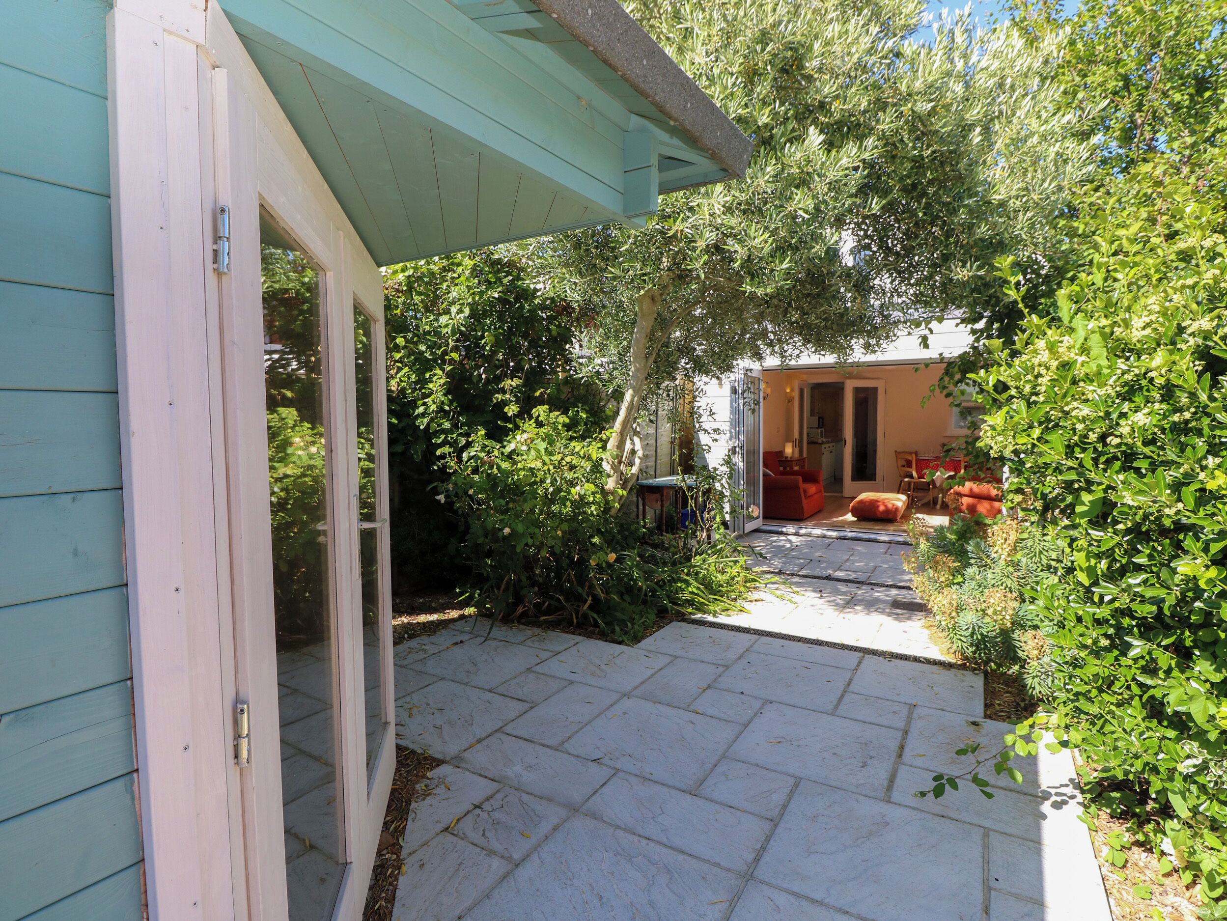 A patio with a stone floor, surrounded by greenery and a building with a door.