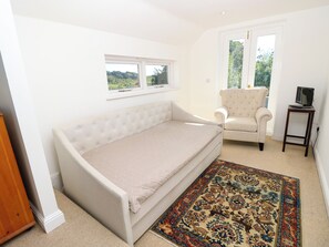 A single-bed room with a window, a chair, a small table with a TV, and a patterned rug. - Merrilees (Yarmouth)
